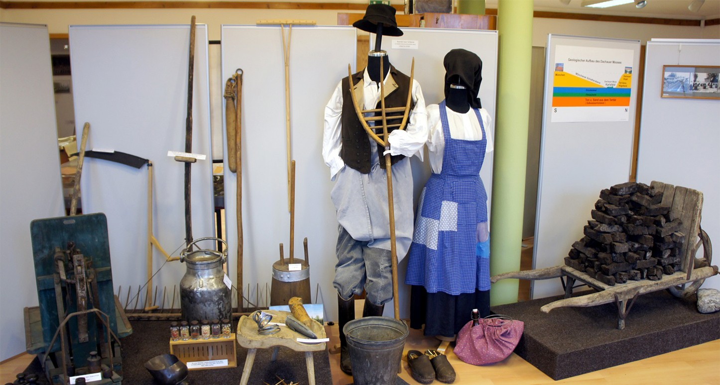 Alte landwirschaftliche Geräte, wie u.a. Rechen, Dreschflegel, Milchkanne und Torfkarre sowie ein bäuerlich gekleidetes Puppenpaar.