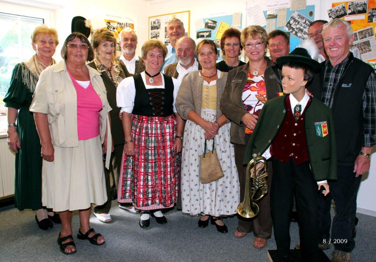 Gruppenbild, im Vordergrund ist eine Kinderschaufensterpuppe im Outfit der Karlsfelder Musikgruppen mit Trompete zu sehen.