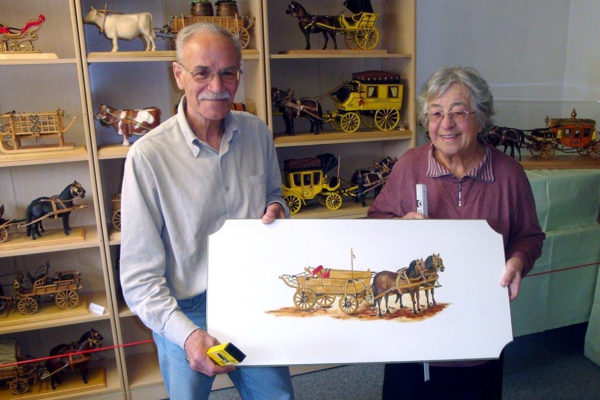 Die Museumsleiterin Ilsa Oberbauer und Georg Stein mit einer Kutschenzeichnung, vor Vitrinen in denen Kutschenmodelle ausgestellt sind.