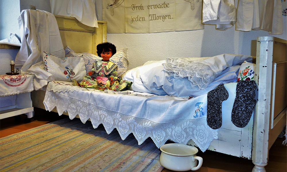 Bett mit Paradekissen, Nachttopf und verschiedenen Wäschestücken